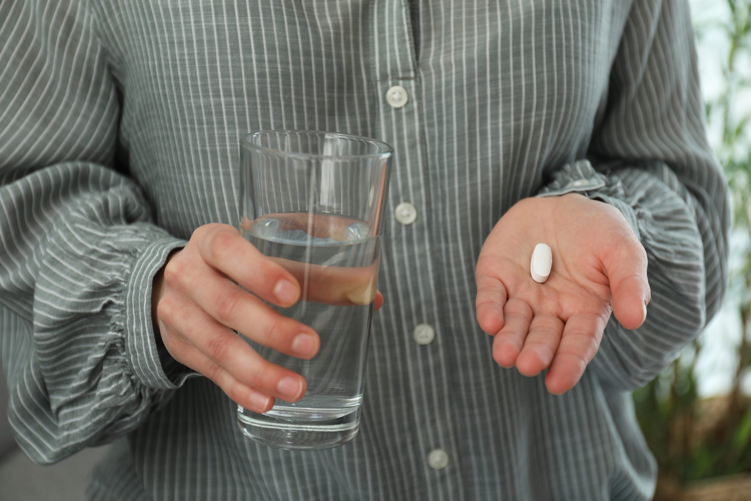 Young Woman With Abortion Pill And Glass Of Water On Blurred Bac